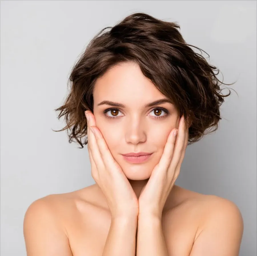 A woman with glowing skin holding her hands to the sides of her face